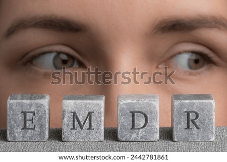 Letters EMDR written on grey stone cubes blocks. Close-up woman's face with eyes looking left. Eye Movement Desensitization and Reprocessing psychotherapy treatment concept. Royalty-Free Stock Photo #2442781861