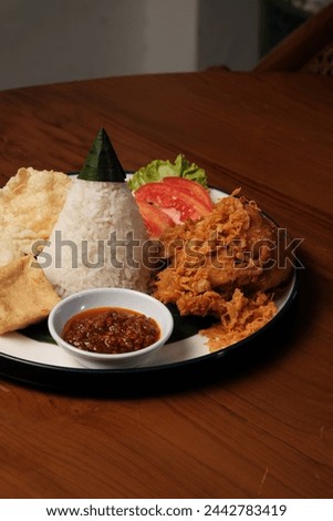 Nasi Tumpeng Ayam Goreng is a traditional Indonesian dish that presents a delicious combination of flavors and textures. The heart of this dish is the cone-shaped rice, known as "nasi tumpeng", Royalty-Free Stock Photo #2442783419