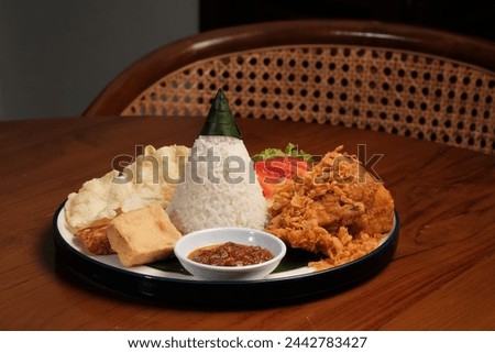 Nasi Tumpeng Ayam Goreng is a traditional Indonesian dish that presents a delicious combination of flavors and textures. The heart of this dish is the cone-shaped rice, known as "nasi tumpeng", Royalty-Free Stock Photo #2442783427
