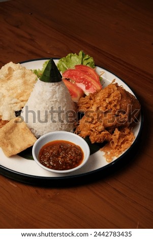 Nasi Tumpeng Ayam Goreng is a traditional Indonesian dish that presents a delicious combination of flavors and textures. The heart of this dish is the cone-shaped rice, known as "nasi tumpeng", Royalty-Free Stock Photo #2442783435