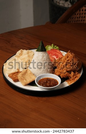 Nasi Tumpeng Ayam Goreng is a traditional Indonesian dish that presents a delicious combination of flavors and textures. The heart of this dish is the cone-shaped rice, known as "nasi tumpeng", Royalty-Free Stock Photo #2442783437