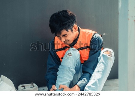 Asian HVAC engineer suffered serious leg injury on the job. Urgent first aid and assistance from coworkers is essential. Expressions of pain on face convey physical and emotional response. Royalty-Free Stock Photo #2442785329