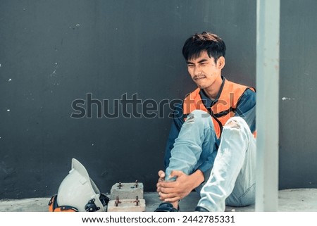 Asian HVAC engineer suffered serious leg injury on the job. Urgent first aid and assistance from coworkers is essential. Expressions of pain on face convey physical and emotional response. Royalty-Free Stock Photo #2442785331