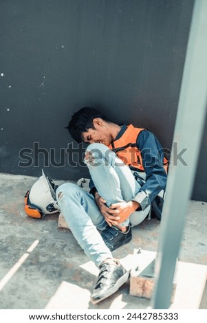 Asian HVAC engineer suffered serious leg injury on the job. Urgent first aid and assistance from coworkers is essential. Expressions of pain on face convey physical and emotional response. Royalty-Free Stock Photo #2442785333