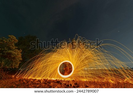 reflection of spark fire swirl from steel wool with long exposure speed motion abstract at twilight on the sea. 
Sparks of light bounces off the water in reflected lines.
dark sky background.
