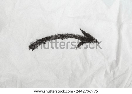Arrow pointing downward to the right , scribbled with black ink on white crumpled paper texture