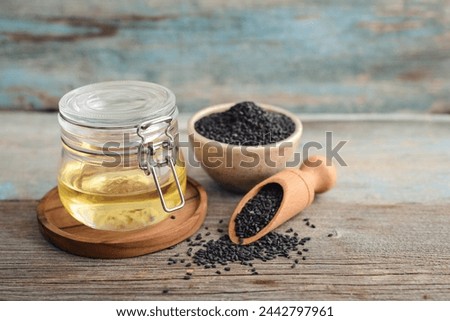 Black sesame seeds in bowl and oil in glass jar on wooden background closeup. Royalty-Free Stock Photo #2442797961