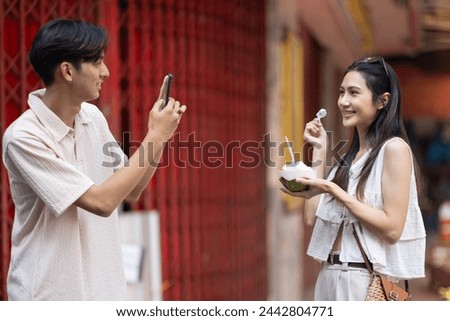 Asian tourists taking pictures with friends eating ice cream and walking on street food in market at Thailand.