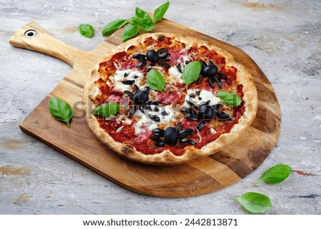 Traditional Italian Halloween spider pizza with salami, mozzarella and olives served as close-up with bat and ghosts on a wooden pizza shovel 
