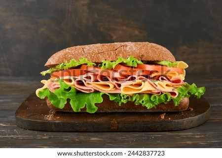 Sandwich. One fresh big submarine sandwich with ham, cheese, lettuce, tomatoes and microgreens on old wooden dark background. Healthy breakfast theme concept, school lunch, breakfast or snack. 