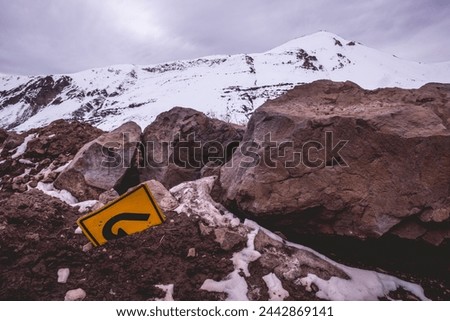 A turn in the cold: a solitary "u turn" sign lost in the snow and rocks of a snowed mountain peak