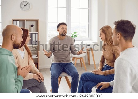 Professional psychotherapist leading group of young adults, helping male and female patients to cure mental health problems through group therapy activities. Group therapy session concept.  Royalty-Free Stock Photo #2442888395