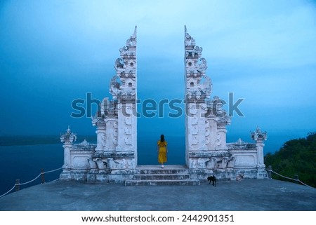 A woman in a yellow dress stands at a famous Balinese traditional gate on the island of Nusa Penida