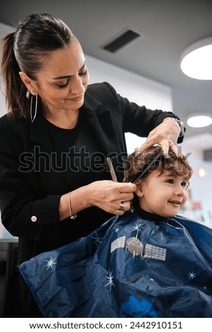 Woman hairdresser cutting a child's hair with comb and scissors in a salon