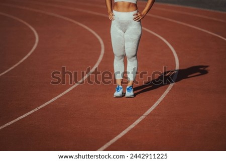 Cropped picture of an unrecognizable sportswoman standing on running track on stadium with shadow behind her. Runner's legs standing on stadium. A fit confident sportswoman preparing for marathon.