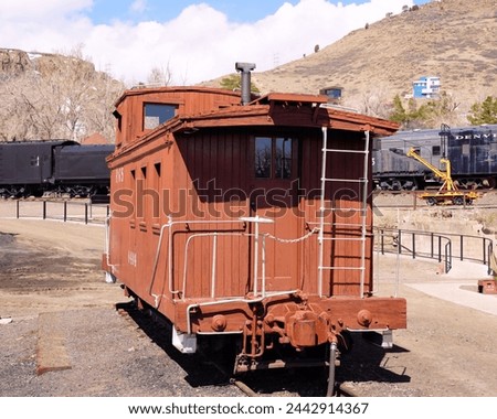 A Red Wooden Narrow Gauge Caboose in a Train Yard Royalty-Free Stock Photo #2442914367