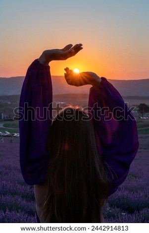 Woman raises arms in lavander field at sunset enjoys sunset in purple flower field. Serene floral setting. Setting sun. Conveying peaceful ambiance in flower field at sunset