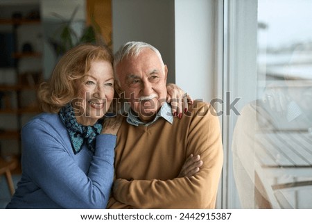 Happy mature couple looking through window at home.	