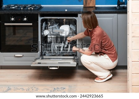 Busy housewife putting dirty plates in dishwasher machine in the kitchen. Household and exhausting cleaning day concept Royalty-Free Stock Photo #2442923665