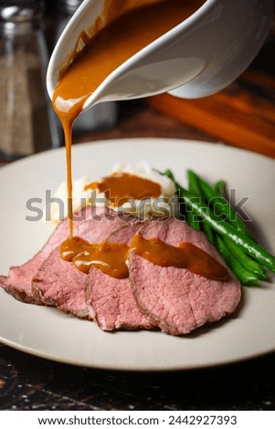  pouring brown gravy sauce on roasted beef Royalty-Free Stock Photo #2442927393