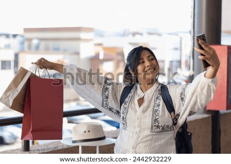 Horizontal photograph with copy space of a brown skin woman smiling and taking selfies with her mobile phone, on the balcony of some stores in Mexico where she buys merchandise during her trip
