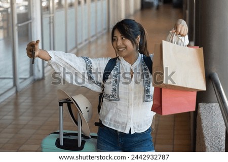 Horizontal photograph with copy space of a woman in her 20s, goes shopping at a mall to buy as a customer and takes selfies with her phone with her bags of merchandise while traveling