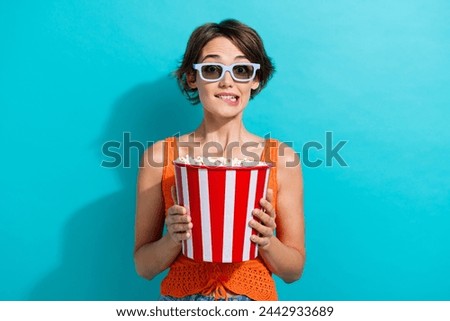 Portrait of nervous girl with short hairdo wear orange knit top in 3d glasses biting lip hold popcorn isolated on blue color background