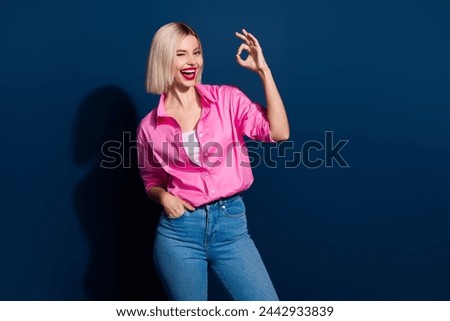 Photo of adorable woman with bob hairstyle dressed pink shirt showing okey blinking eye arm in pocket isolated on dark blue background