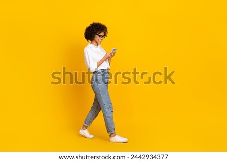 Full length body size view of attractive trendy cheerful girl going using gadget chatting isolated over vivid yellow color background