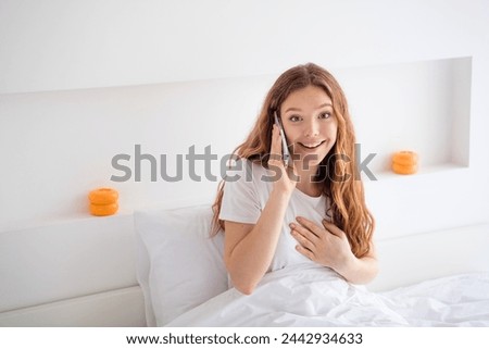 Photo of cheerful pretty girl sit comfy bed hand touch chest chatting telephone free time weekend bedroom indoors