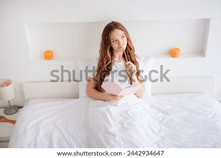 Photo of minded pensive girl sit bed under blanket hold pen notepad look curious away ponder decide bedroom inside