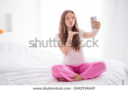 Full body photo of lovely girl sit cozy bed hold smart phone make selfie hand send air kiss bright interior bedroom indoors