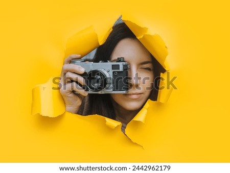 A young paparazzi girl with a rare SLR camera looks out from her hiding place and carefully watches what is happening. Yellow paper hole.Tabloid press.Looking for a subject for stock photos