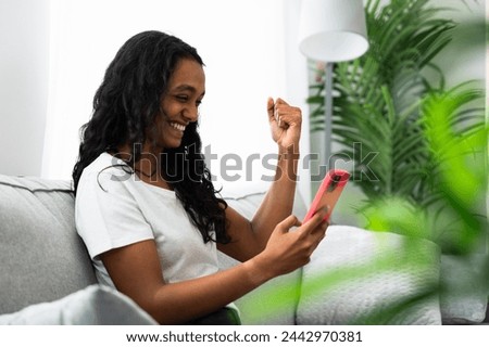 Young Indian woman celebrating good results while looking at mobile phone.