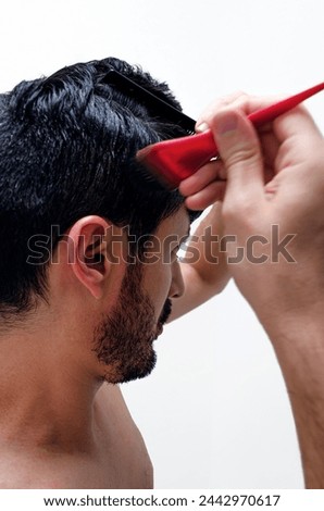 Young man applying natural hair dye with red brush to cover his gray hair. Dark brown henna based hair dye. Profile view with white background.