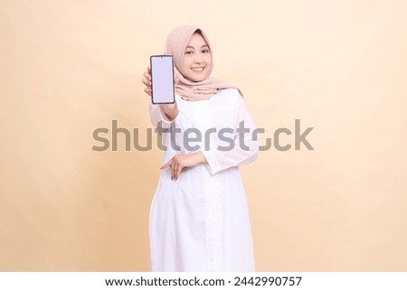 girl asian muslim wearing a hijab, smiling cheerfully, holding a cellphone gadget in her hand in front of her with her arms crossed. Lifestyle, business and finance concept