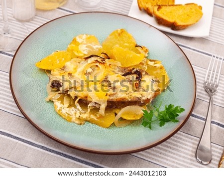 Appetizing browned pork steaks and slices of potatoes smothered with onions in creamy cheesy sauce. Homemade comfort food.. Royalty-Free Stock Photo #2443012103