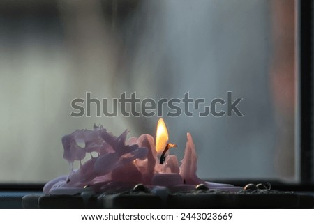 Burning candle on a window sill with smoke in the background.