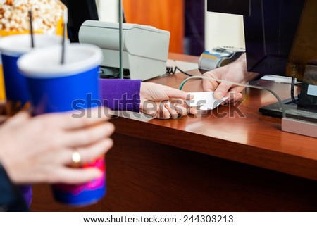 Cropped image of women holding drinks while buying movie tickets from seller at box office Royalty-Free Stock Photo #244303213