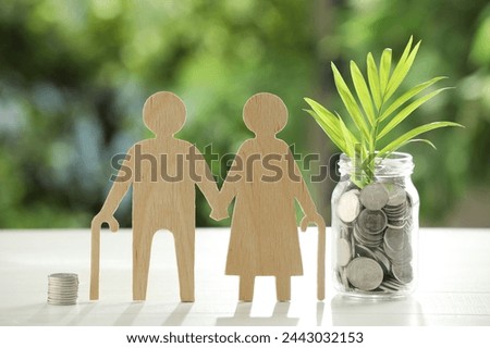 Pension savings. Figure of senior couple, jar with coins and twig on white table against blurred green background