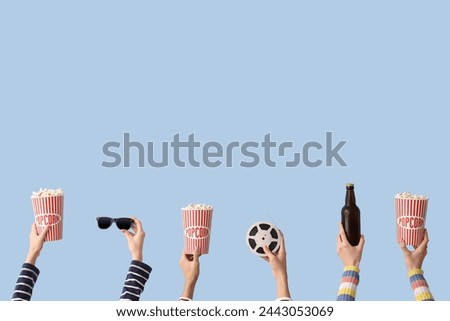 Many hands with buckets of popcorn, beer and film reel on blue background