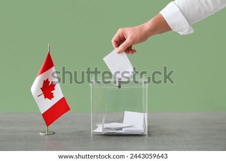 Voting young man with Canadian flag near ballot box on table at polling station, closeup Royalty-Free Stock Photo #2443059643