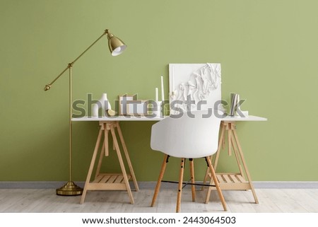 Stylish workplace with candles, blank picture frames and decor near color wall