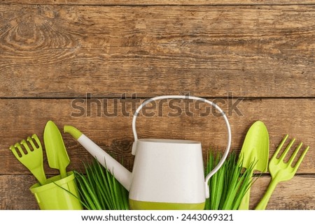 Watering can with gardening tools on wooden background. Top view