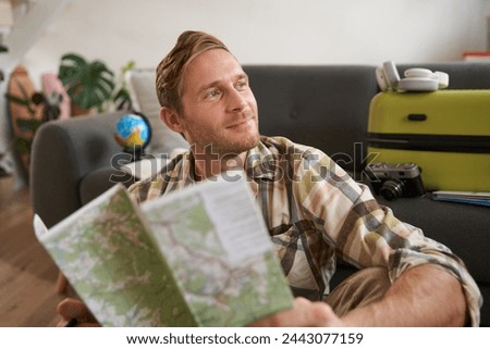 Smiling handsome man with map in hands, packed suitcase, goes on holiday, prepared to go on vacation.