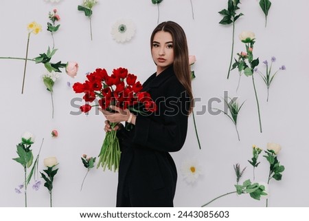 A woman poses with vibrant bouquets of red tulips in hands, fashion outfit. Spring women`s day, 8th of March. Flowers hanging in air