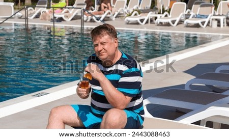 A plump man of European appearance with an alcoholic drink sits by the pool.