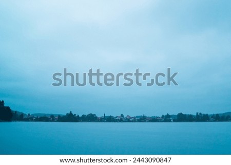 Landscape view with thick cloud cover and rain falling down the blue sky onto a city in the horizon and the river nearby  creating a soft rainy landscape picture on a cold wet autumn day