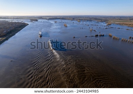 Inland shipping cargo ships passing the extended river IJssel during high water level with flood plains tripling the width of the fast flowing waterway. Dutch flat landscape aerial Royalty-Free Stock Photo #2443104985