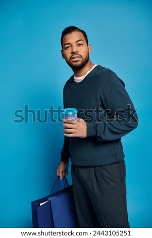 charismatic african american man standing sideways and holding shopping bags with paper cup in hand